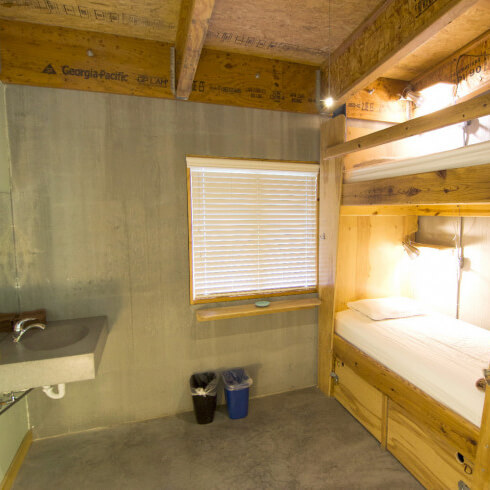 Simple room with bunk bed, window blinds, sink, and trash bins.
