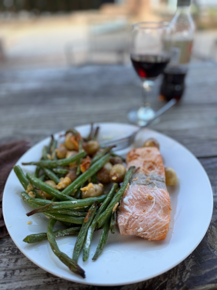 Salmon with green beans and potatoes on a plate, glass of red wine nearby.